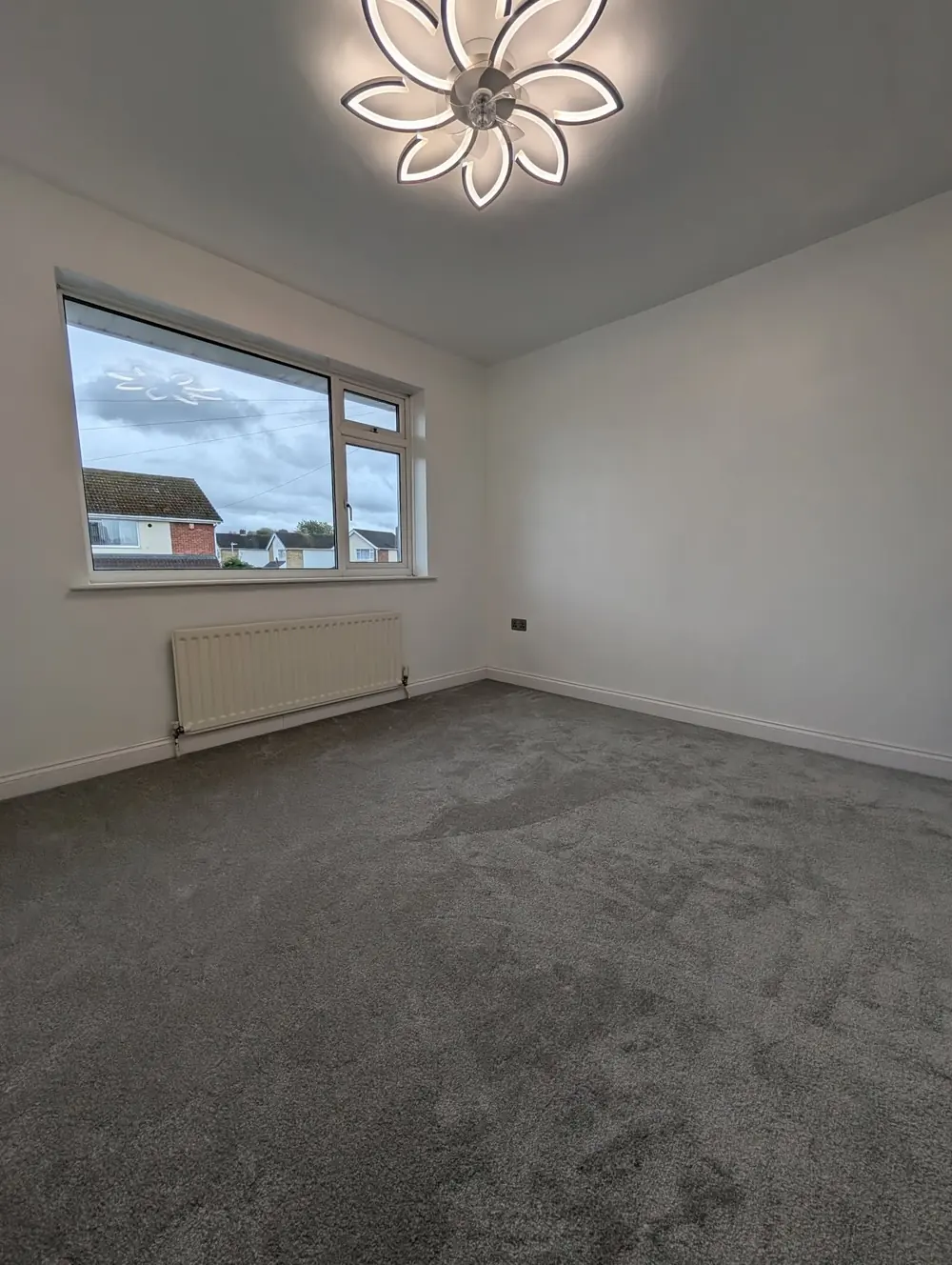Grey twist carpet filling a bedroom with a wide window and a radiator under it.