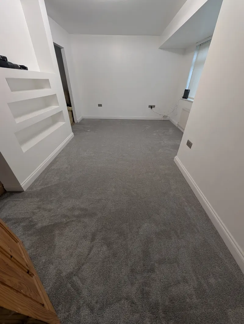 Grey carpet in a lounge with a staircase edge and an alcove, finished up to the skirting.