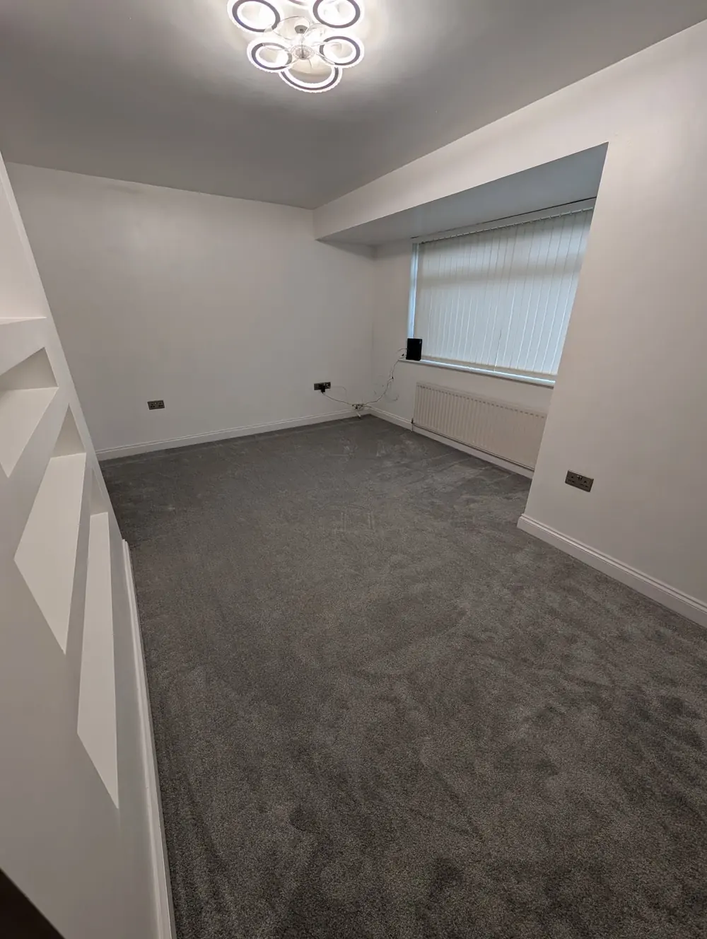 Grey carpet in a through lounge with a chimney breast and alcove, lit by a ceiling light.