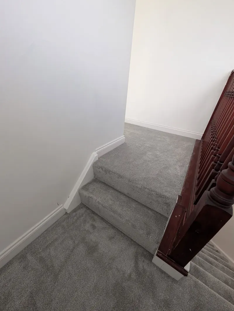Grey carpet fitted around a winder step and up to a landing, past a dark mahogany newel post.