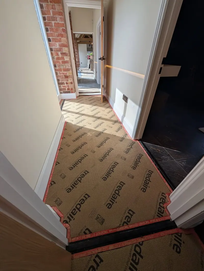 Tredaire underlay cut to shape in a hallway with exposed brick, black gripper strips visible along the edges.