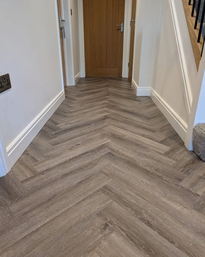 Grey herringbone LVT on a landing, running past a white door and skirting.