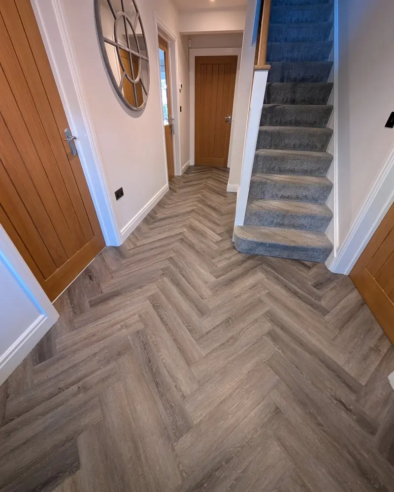 Grey herringbone LVT in a hallway leading to a carpeted staircase and an oak panelled wall.