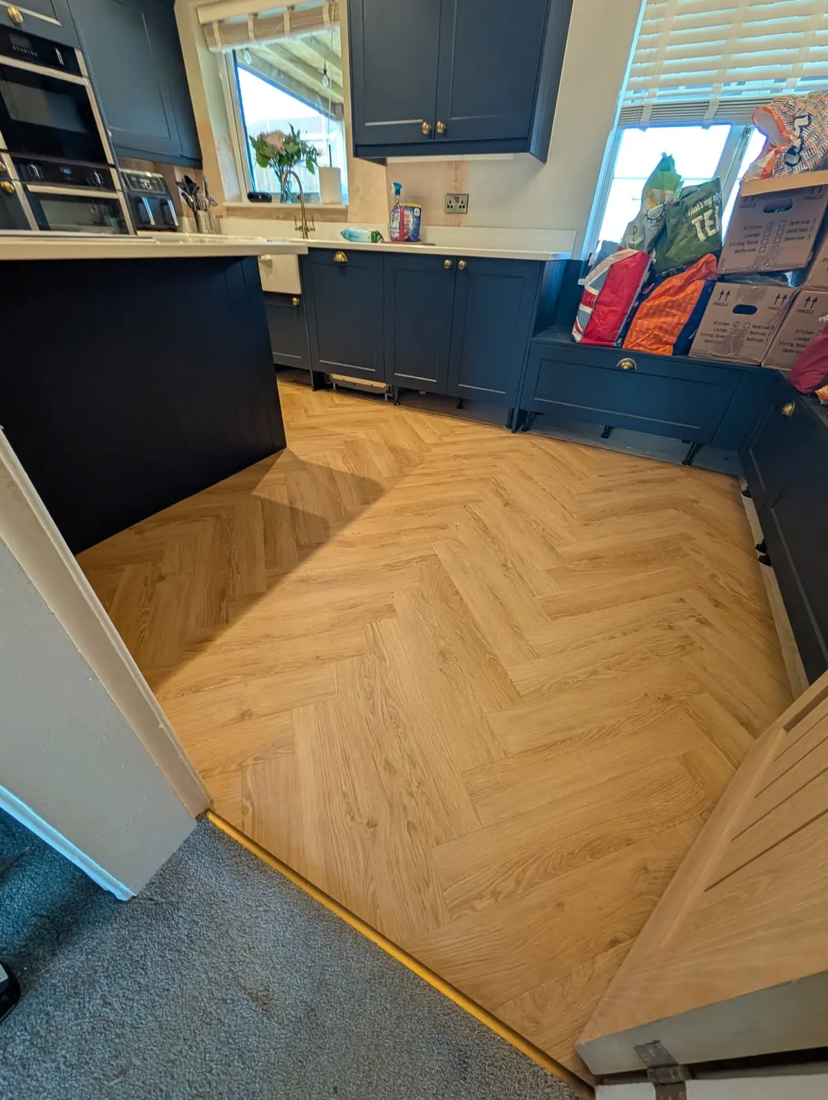 Natural oak herringbone LVT across a kitchen diner with navy units and a dark island.