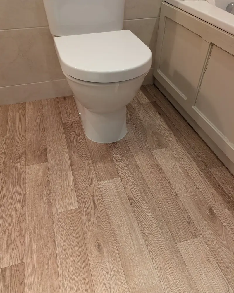 Pale wood effect plank flooring fitted tight around a toilet pan in a cloakroom.