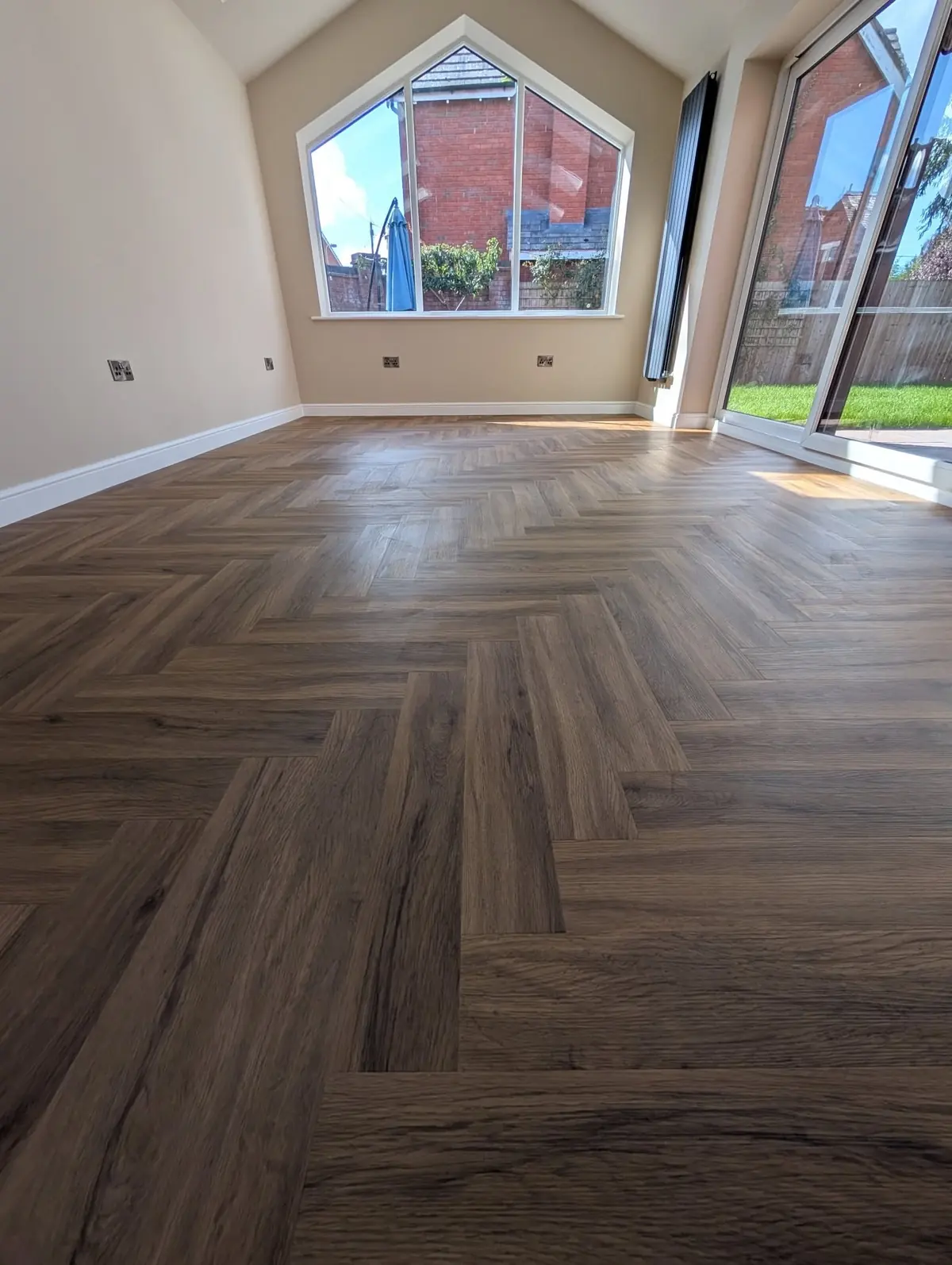 Walnut herringbone LVT in a bright room with a wide apex window and bifold doors to the garden.