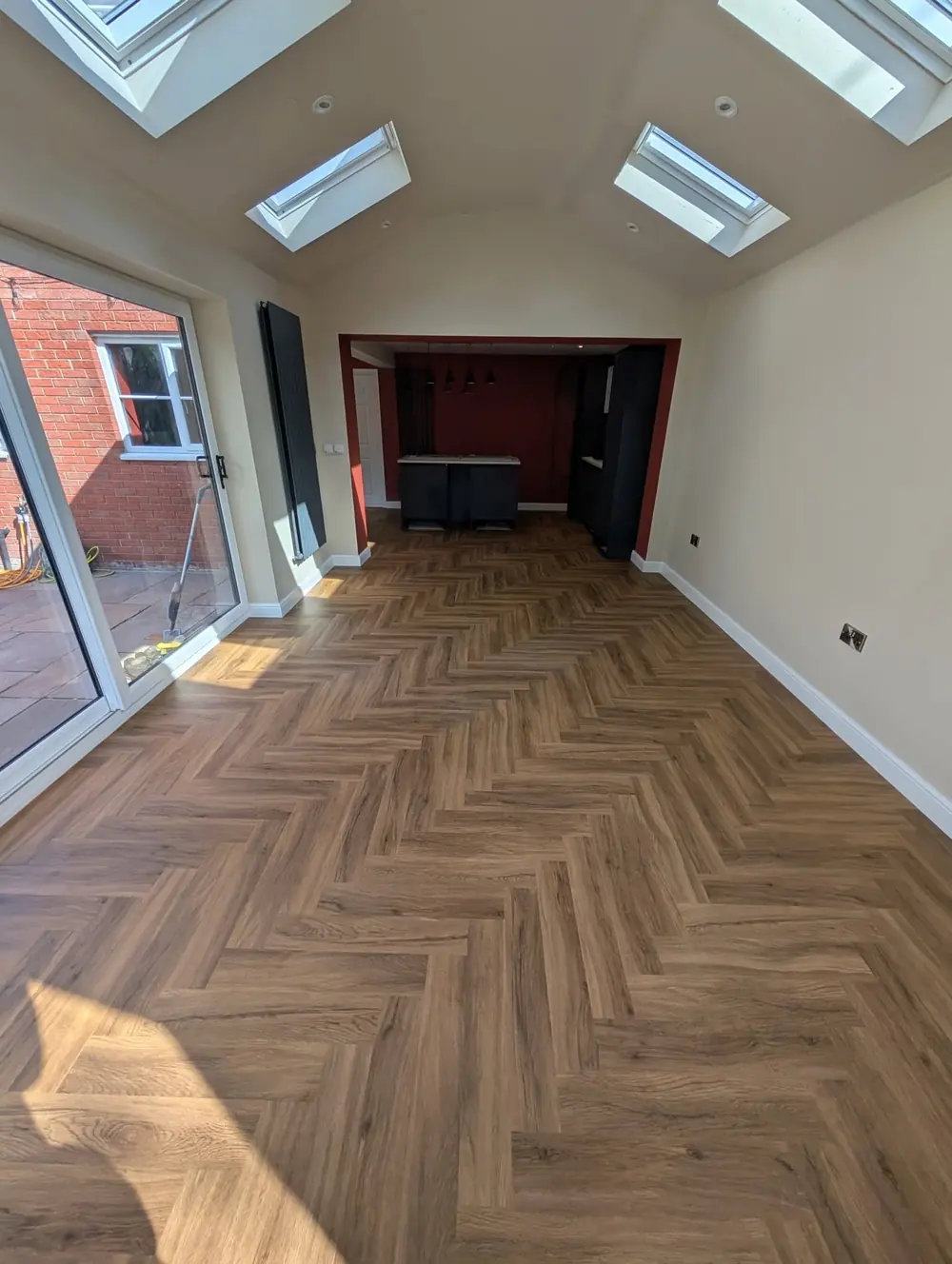 Walnut herringbone running the length of an open plan room towards a dark fireplace recess under two roof lights.