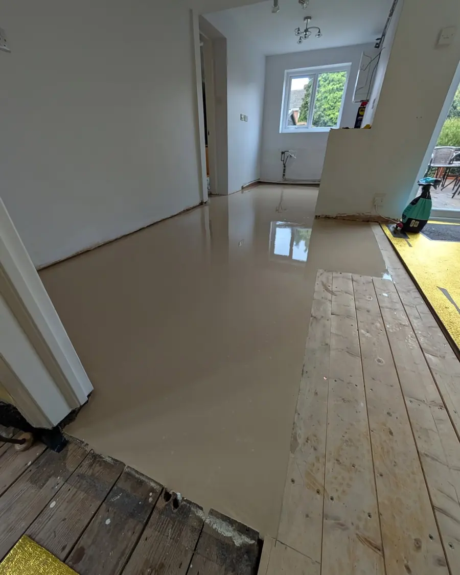 Cream latex screed poured over part of a floor with bare timber boards and a trowel still on the untreated section.
