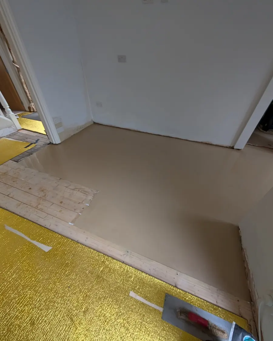 A cured cream latex screed surface running up to a wall, with a trowel and a yellow underlay offcut at the edge.