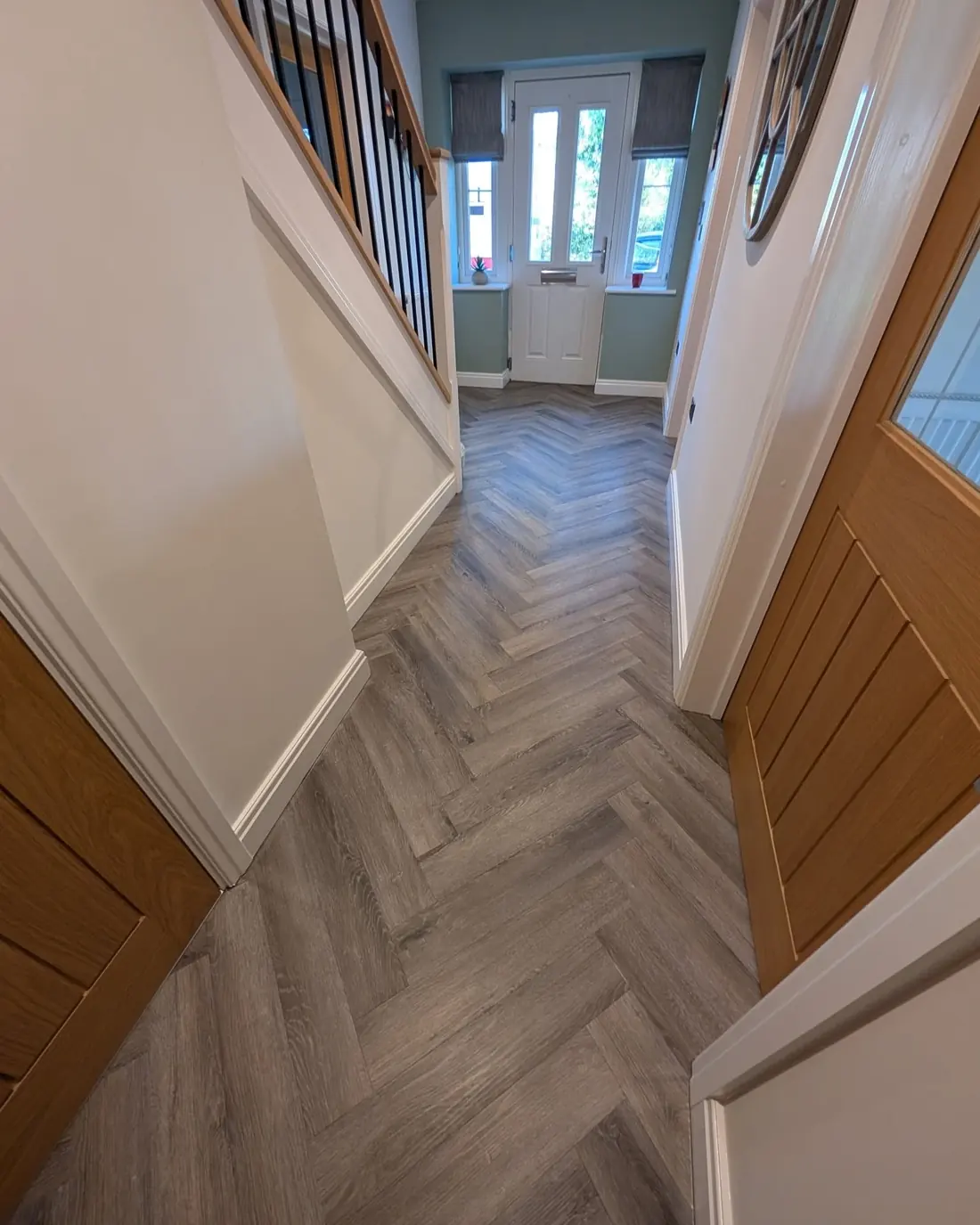 Finished grey herringbone hallway with oak doors, white walls and black staircase spindles.