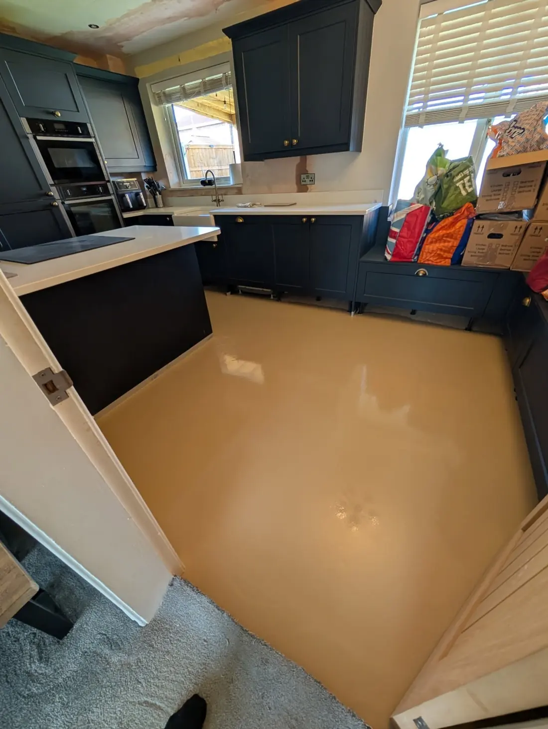 Wet cream latex screed poured across a navy kitchen floor, still glossy before it cures.