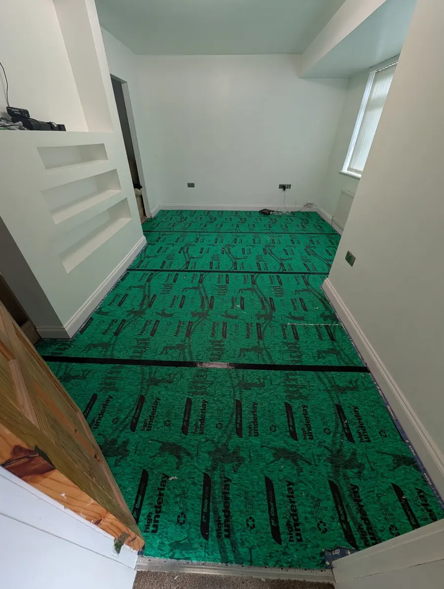 Bright green underlay taped down across a stripped room with alcove shelving.