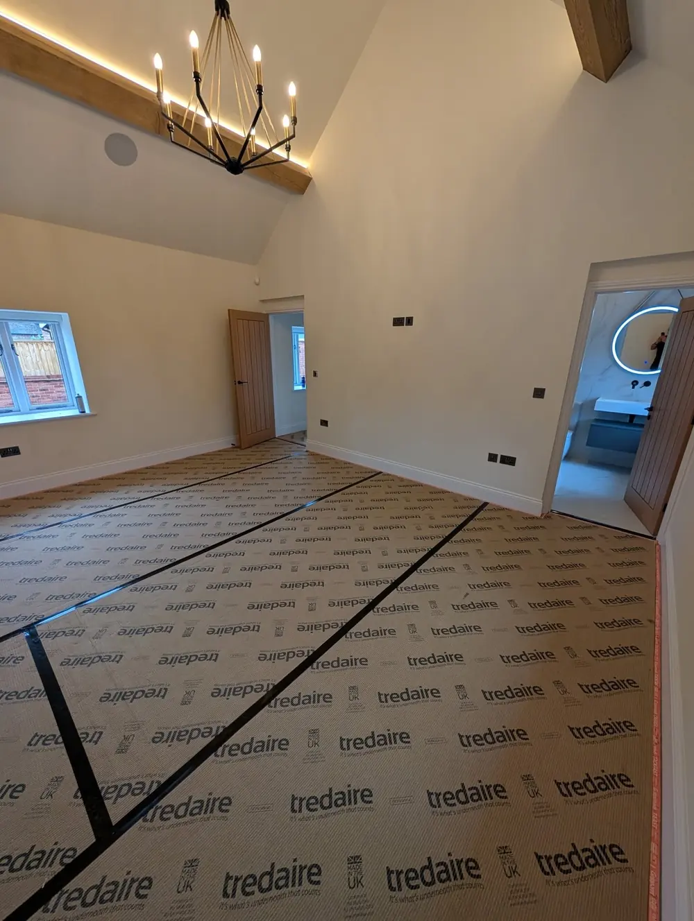 Tredaire underlay laid out across a room with black gripper strips fixed around the edges, under a vaulted ceiling with oak beams.