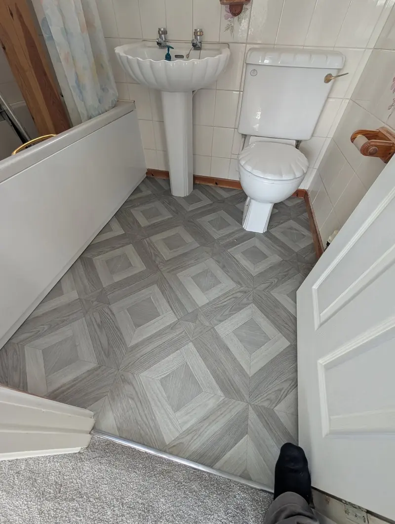 Grey and beige diamond pattern vinyl fitted in a cloakroom around a basin pedestal and toilet.