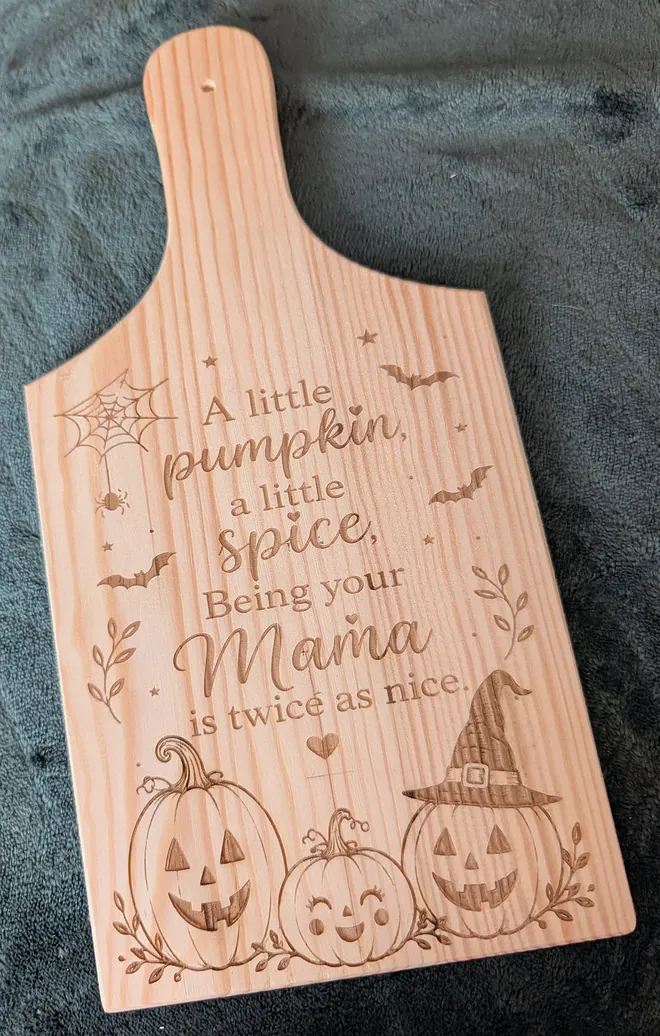 Her photo of the finished pine board: the same words, pumpkins and bats engraved into the wood, the grain running through every letter.