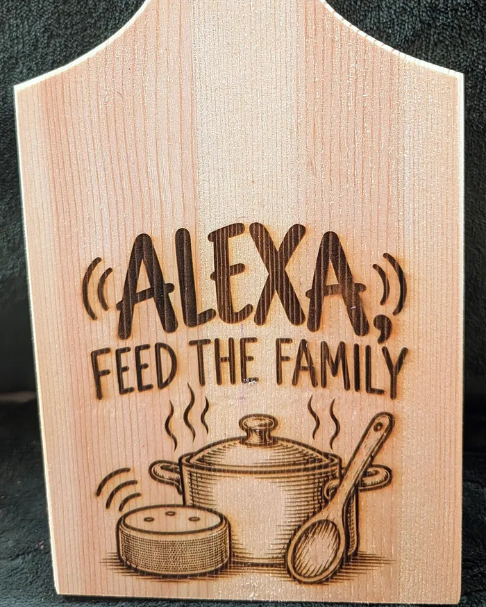 A wooden chopping board engraved 'Alexa, Feed the Family' with a cooking pot and spoon.