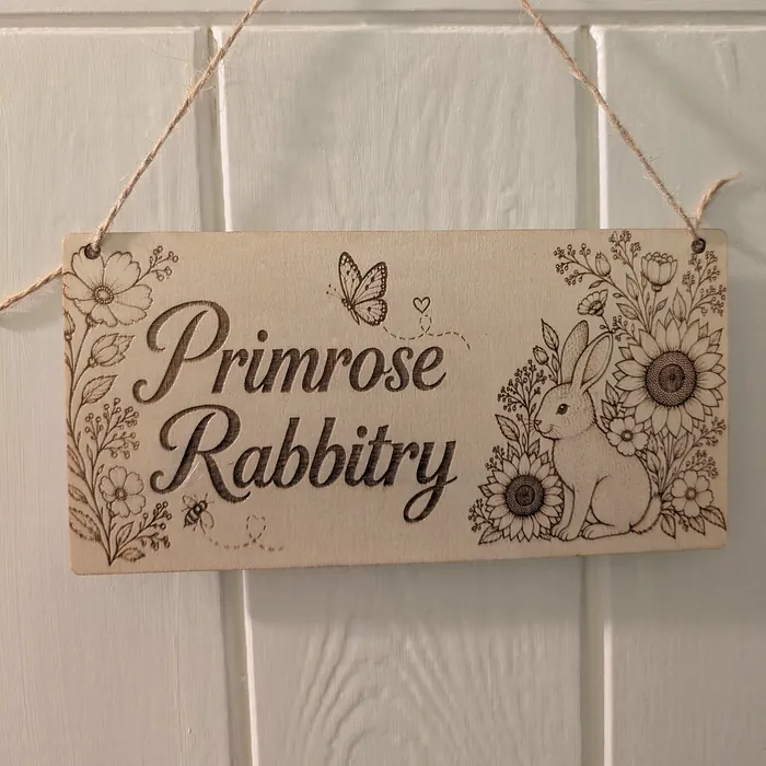 A hanging wooden sign for 'Primrose Rabbitry' engraved with a rabbit, sunflowers and a butterfly.