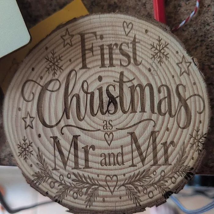 A finished log slice with its bark rim and red and white twine, engraved 'First Christmas as Mr and Mr' with two rings and snowflakes.