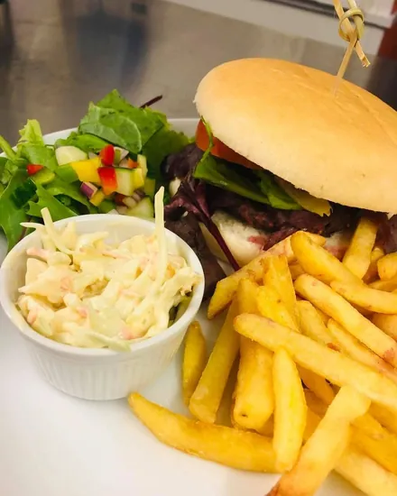 A burger in a bun with chips, a pot of coleslaw and a side salad on a white plate.