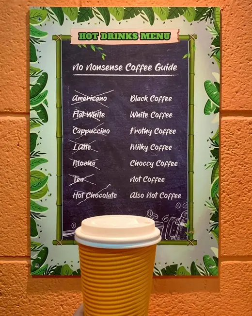 The hand written hot drinks chalkboard headed No Nonsense Coffee Guide, on the orange wall by the counter.