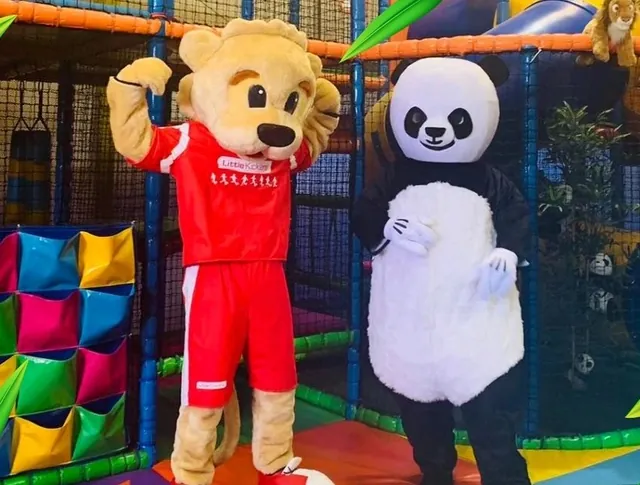 The Panda-Monium panda mascot in a red bib beside a brown bear mascot in a red football shirt, on the rainbow play floor.