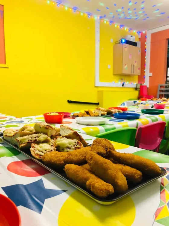 A party table with hot food including chicken goujons, on a star print cloth.