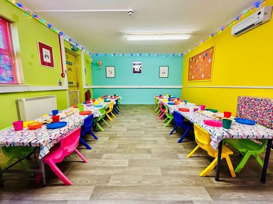 The Den set for a party: two long tables in confetti cloths, rainbow chairs, bunting lights, and lime and yellow walls.