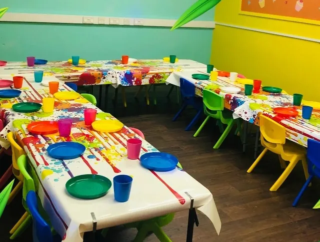 The Den set up with long tables in confetti cloths and rainbow chairs, against lime and yellow walls.