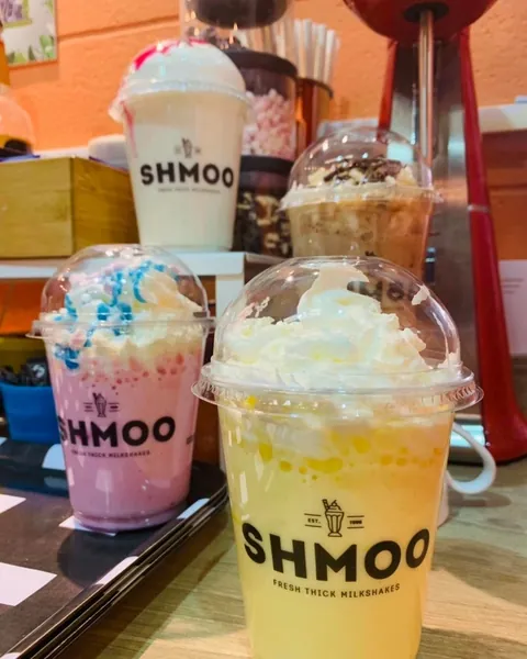 Three Shmoo milkshakes in domed cups topped with whipped cream, on the wooden counter.