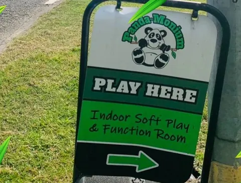 The Panda-Monium A board on the grass outside, reading Play Here, Indoor Soft Play and Function Room, with an arrow.