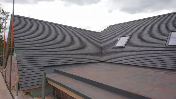 A flat roof with a trimmed upstand, set between steep slopes of dark plain tiles with roof windows.