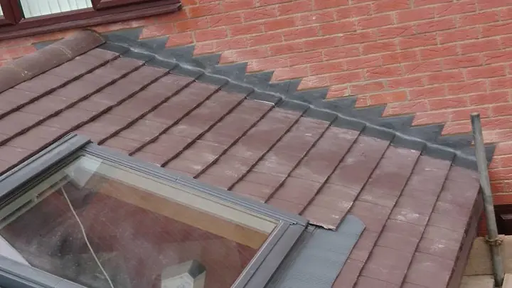 A roof window set into red-brown plain tiles, with stepped lead flashing along the brick wall above it.