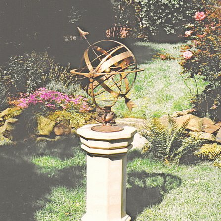 A Taurus armillary mounted on an Upton pedestal, seen from a distance in its garden setting.