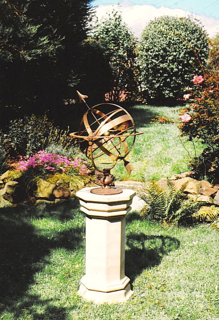 A Taurus armillary mounted on an Upton pedestal, seen from a distance in its garden setting.