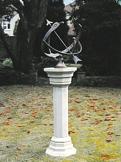 A Draco armillary on a tall fluted Brympton pedestal, standing on a lawn scattered with fallen autumn leaves.