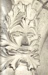 A traditional Green Man carved in stone, a face peering out from a mask of deeply cut leaves, of the kind found in village churches and cathedrals.
