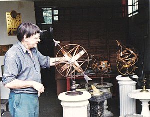 Robert Foster standing in the workshop doorway, holding up a brass armillary sphere, with two more armillaries on pedestals beside him.