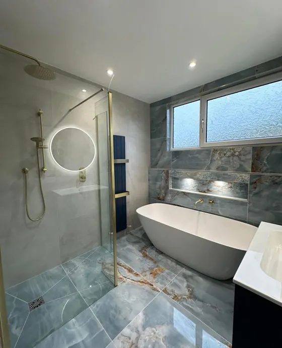 Bathroom with a freestanding bath, blue and gold veined marble effect floor and a round backlit mirror