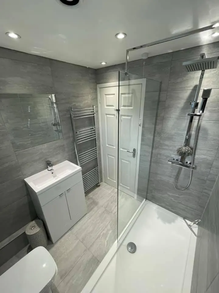 Bath with a glass shower screen, grey tiling and a white basin unit