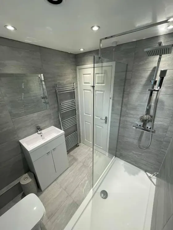Bath with a glass shower screen, grey tiling and a white basin unit