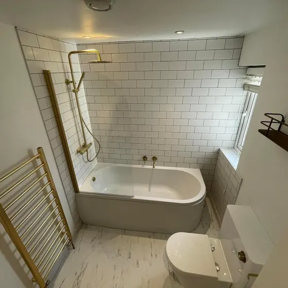 Bath with a brass shower over it, white metro tiling and a brass towel rail