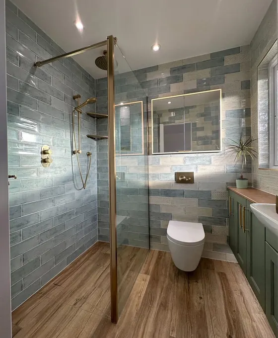 Shower with brass fittings, blue green tiling, wood effect flooring and a green vanity unit