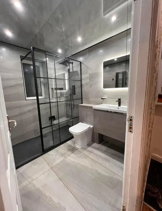 Bathroom with a black framed shower screen, a wall hung vanity unit and a backlit mirror