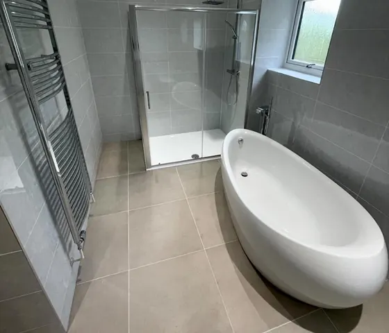 Freestanding oval bath against large format grey tiling with a chrome towel rail