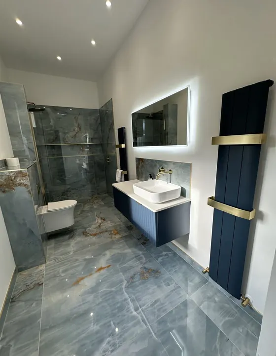 Bathroom with green and gold veined marble effect tiling, a navy radiator and a wall hung basin