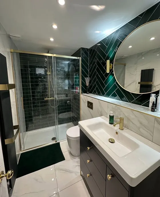 Bathroom with dark green tiling, brass fittings, a large round gold framed mirror and a black vanity unit