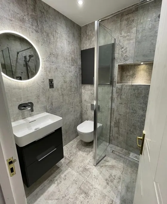 Walk in shower with grey marble effect tiling, a round backlit mirror and a dark vanity unit