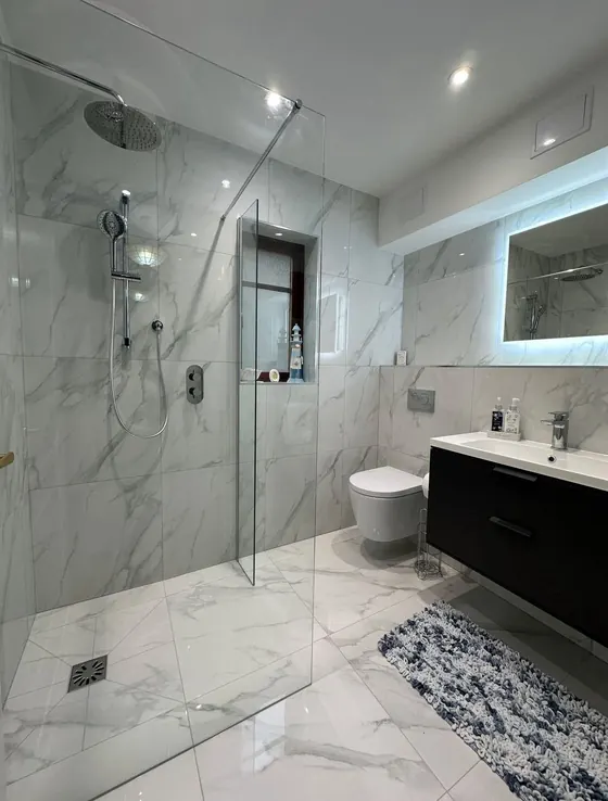 Walk in shower with marble effect tiling, a black vanity unit and a backlit mirror