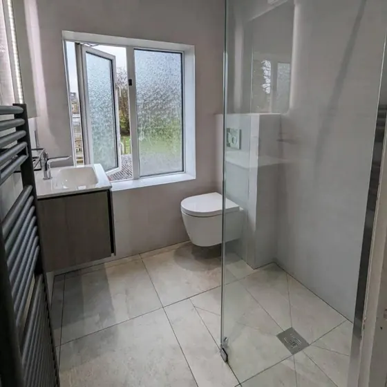 Level access wet room with a linear floor drain, glass screen and a black heated towel rail