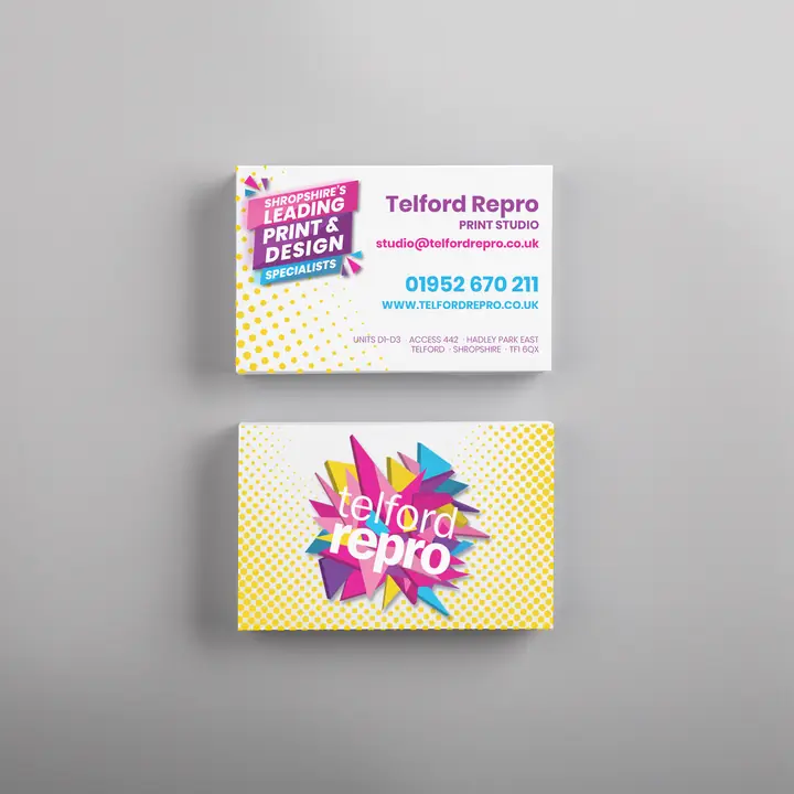 Two stacks of Telford Repro business cards on a grey surface. The front reads Telford Repro Print Studio with the studio email address and 01952 670 211, next to a magenta and violet flash reading Shropshire's leading print and design specialists. The back carries the shard burst logo on a yellow halftone dot pattern.